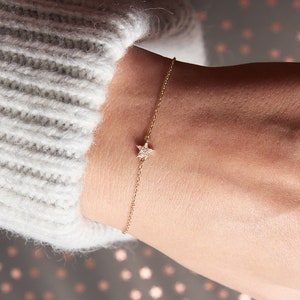 May include: A delicate gold chain bracelet with a small, sparkling star charm. The star is set with tiny diamonds.