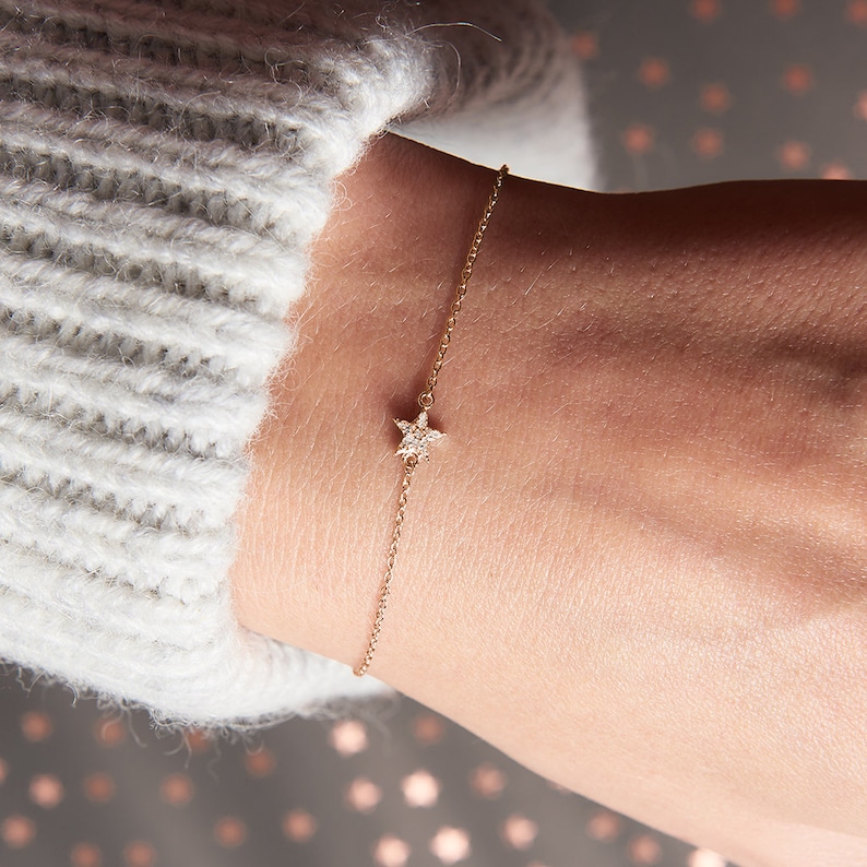 May include: A delicate gold chain bracelet with a small, sparkling star charm. The star is set with tiny diamonds.