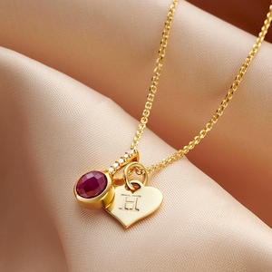 May include: Gold necklace with a heart charm and a red gemstone pendant. The heart charm has the letter "H" engraved on it.
