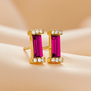 Peut inclure: Une paire de boucles d'oreilles en or avec une pierre rectangulaire rose sertie dans chaque boucle d'oreille. Les pierres sont entourées de pierres claires plus petites.
