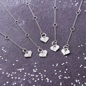 May include: Four silver necklaces with heart-shaped pendants. Each pendant has a different letter engraved on it: A, J, L, and C.
