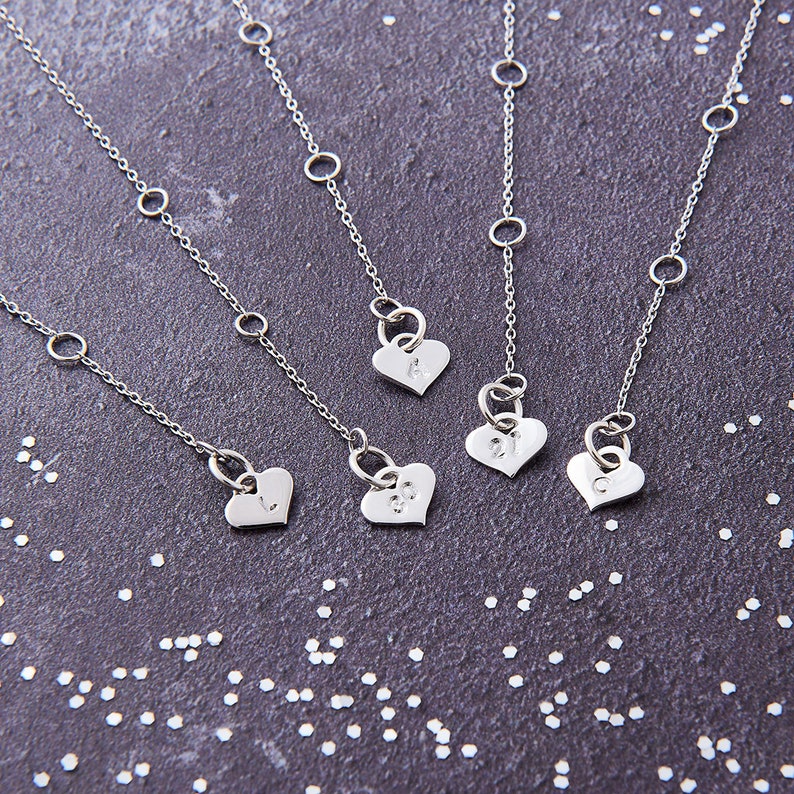 May include: Four silver necklaces with heart-shaped pendants. Each pendant has a different letter engraved on it: A, J, L, and C.