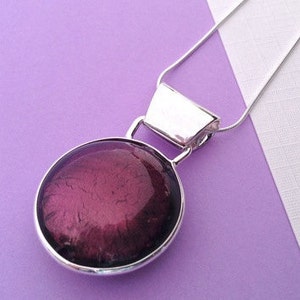 May include: A silver pendant necklace with a large, round, dark purple glass pendant.