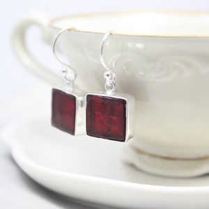 May include: A pair of silver dangle earrings with square red glass stones.