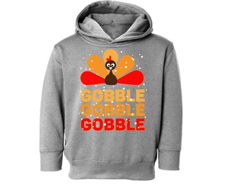 Op de afbeelding: Grijs hoodie met een cartoon kalkoen en de tekst "Gobble Gobble Gobble" in oranje en rood.