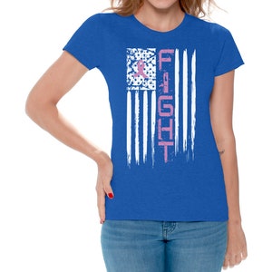 May include: A royal blue t-shirt with a distressed white American flag design. The flag has a pink ribbon in the upper left corner and the word "FIGHT" vertically down the right side.
