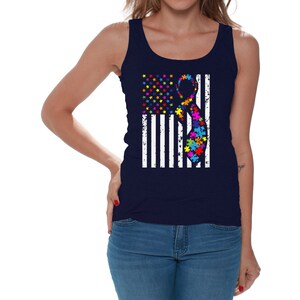 May include: A navy blue tank top with a white distressed American flag design. The flag has a colorful puzzle piece ribbon in the center.