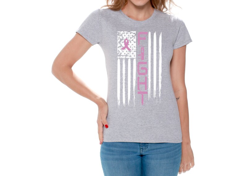 May include: A gray t-shirt with a white distressed American flag design. The flag has a pink ribbon in the upper left corner and the word "FIGHT" written vertically down the right side.