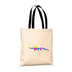 Può includere: Una borsa tote in tela beige con manici neri. La borsa presenta una silhouette di dinosauro colorata composta da pezzi di puzzle in tonalità blu, giallo, rosa e bianco.