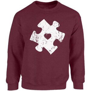 May include: A maroon sweatshirt with a white distressed jigsaw piece design featuring a small heart in the centre.