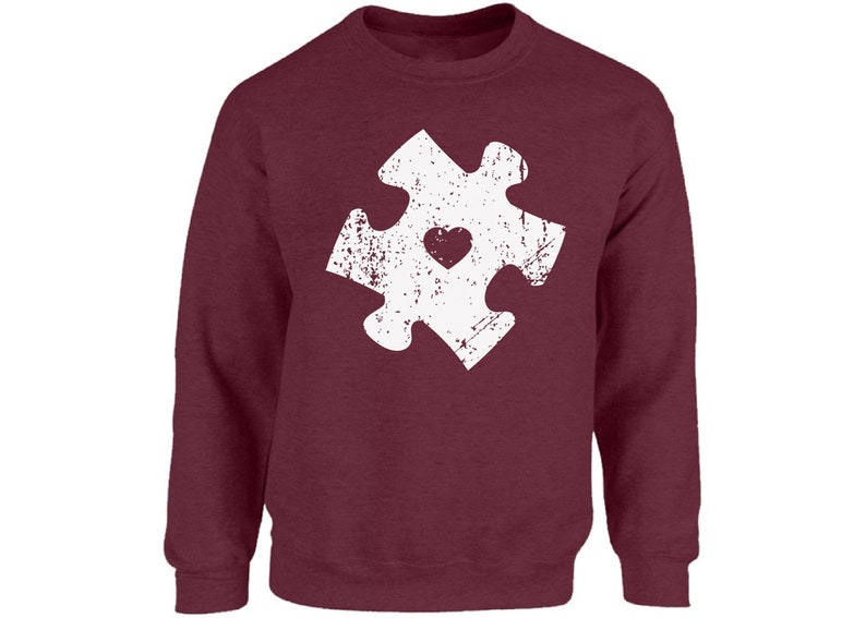 May include: A maroon sweatshirt with a white distressed jigsaw piece design featuring a small heart in the centre.