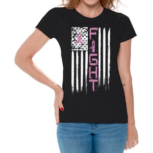 May include: Black t-shirt with a distressed American flag design. The flag is white and black with a pink ribbon in the top left corner. The word "FIGHT" is written vertically down the right side of the flag.