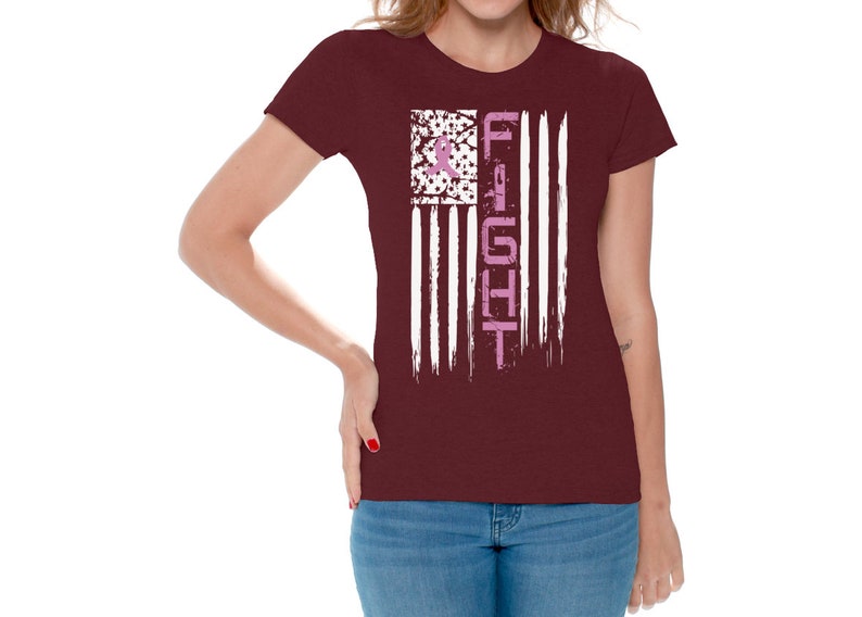May include: A maroon t-shirt with a white and pink American flag design. The flag has the word "FIGHT" written vertically down the right side. The flag is distressed and has a pink ribbon in the top left corner.