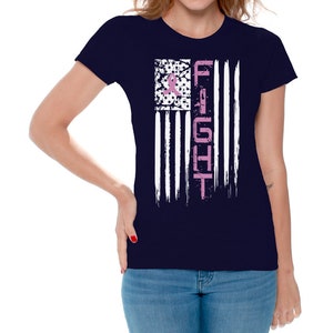 May include: Navy blue t-shirt with a white and pink American flag design. The flag has the word "FIGHT" written vertically down the right side in pink. A pink ribbon is in the top left corner of the flag.