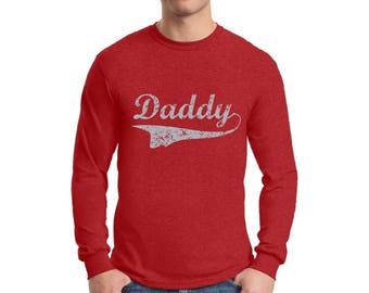 May include: Red long-sleeve shirt with a white distressed graphic that says "Daddy" in a vintage style font.