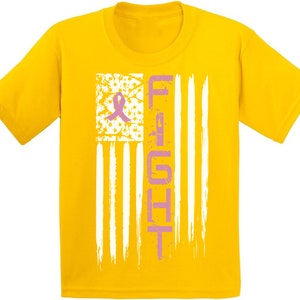 Pu&ograve; includere: Maglietta gialla con un nastro rosa e la parola "FIGHT" stampata su un design di bandiera americana bianca e blu.