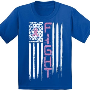 Pu&ograve; includere: Una maglietta blu reale con un design di bandiera americana usurato. La bandiera &egrave; bianca con un nastro rosa e la parola "FIGHT" scritta verticalmente in rosa.