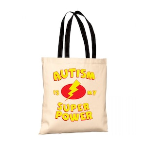 Può includere: Una borsa tote beige con manici neri. La borsa ha una grafica gialla e rossa che dice "L'autismo è il mio super potere" con un fulmine.