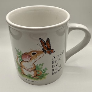 May include: A white ceramic mug featuring a brown mouse with a monarch butterfly on its nose. The text reads, A good friend is a friend forever. The base of the illustration includes the text, 1984 CURRENT, INC. The mug has a curved handle.
