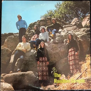 May include: Album cover for "The Random Sample" featuring a group of seven people posing on a rock formation. The album cover has a vintage aesthetic, with the band members dressed in 1960s or 1970s attire. The album title is in yellow text.