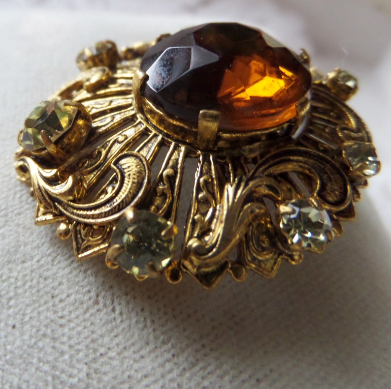 Vintage Round Ornate Gold-tone Brooch With Small Clear Rhinestones And Large Round Faceted Topaz Colored Center Stone