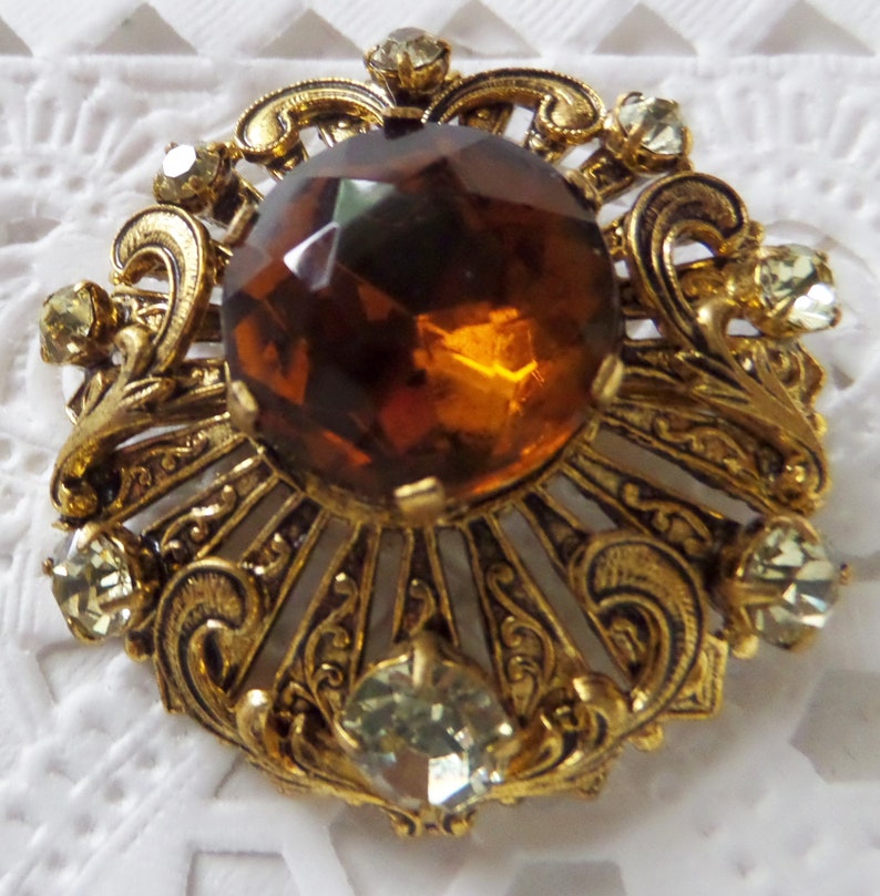 Vintage Round Ornate Gold-tone Brooch With Small Clear Rhinestones And Large Round Faceted Topaz Colored Center Stone