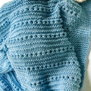 May include: A soft blue knitted baby blanket with a delicate stitch pattern.