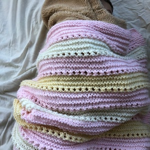 May include: A pink, white, and yellow striped knitted blanket with a brown fuzzy hooded sweater on top.