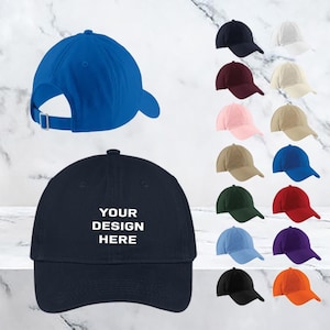 May include: A variety of colors of blank baseball caps. The caps are made of a soft, comfortable fabric and are perfect for customizing with your own design. The text "YOUR DESIGN HERE" is embroidered on one of the caps.