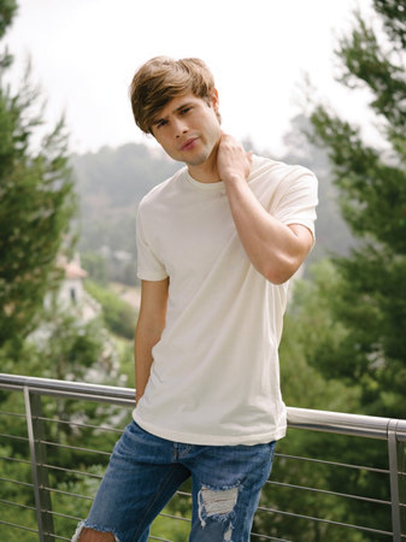 Peut inclure: Un homme portant un t-shirt blanc et un jean bleu. Il se tient devant une balustrade avec un fond vert.