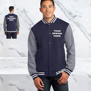 May include: A navy blue and gray varsity jacket with white stripes on the sleeves and collar. The jacket has a button closure and features the text "YOUR DESIGN HERE" embroidered on the left chest.