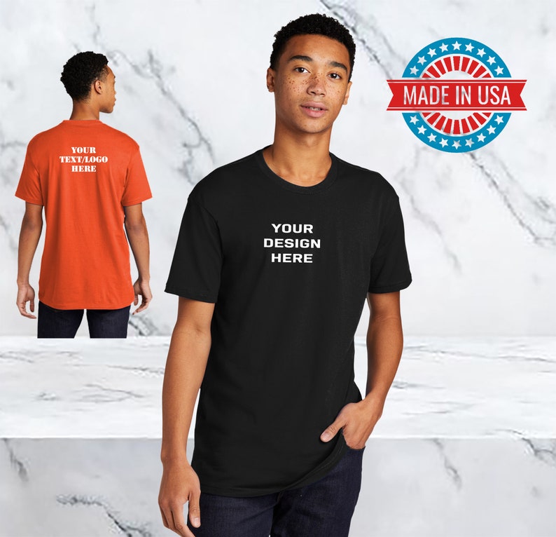 Peut inclure: Un t-shirt noir avec le texte "YOUR DESIGN HERE" en blanc. Le t-shirt est port&eacute; par une personne. L'image comprend &eacute;galement un autocollant en forme d'&eacute;toile rouge, blanc et bleu avec le texte "MADE IN USA".