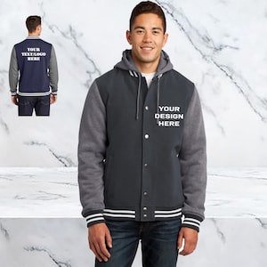 May include: A dark gray hooded varsity jacket with white and gray sleeves and a white stripe around the bottom. The jacket has a button closure and the text "YOUR DESIGN HERE" is embroidered on the front.
