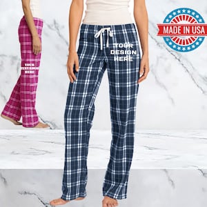 May include: Two pairs of plaid pajama pants. One pair is pink and white, the other is blue and white. Both pairs have a white drawstring and a white text overlay that says "YOUR DESIGN HERE".