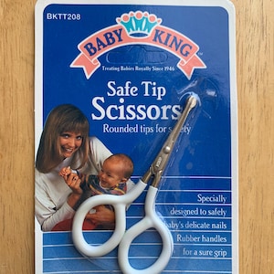 May include: Baby King Safe Tip Scissors on a blue and white card. The scissors have white handles and rounded tips for safety. The card features a photo of a mother and baby, and text that reads "Treating Babies Royally Since 1946."