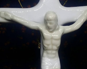 May include: White porcelain figurine of a person on a white cross. The figurine is of a person with arms outstretched, and the cross has a gold string wrapped around it.