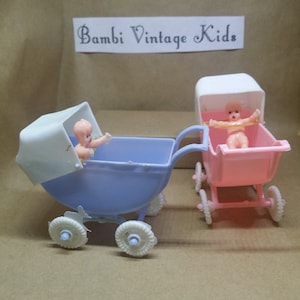 May include: Two vintage toy baby strollers, one blue and one pink, with baby dolls inside. The strollers have white wheels and the dolls have painted faces.