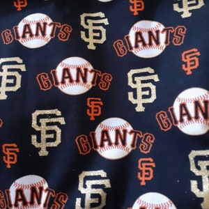 May include: Black fabric with a repeating pattern of baseballs, the word "Giants", and the San Francisco Giants logo. The logo is gold with a red outline and the letters "SF".
