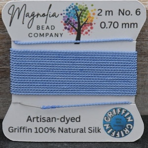 May include: A spool of light blue Griffin 100% Natural Silk thread. The label reads "Magnolia Bead Company", "2 m No. 6", and "0.70 mm". The thread is artisan-dyed and suitable for various crafting projects.