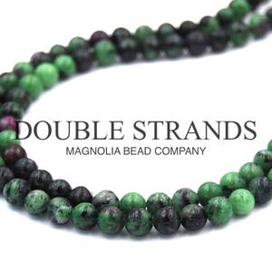 May include: Double strand necklace made of green and black gemstone beads. The necklace is displayed on a white background. The text "DOUBLE STRANDS MAGNOLIA BEAD COMPANY" is visible in the image.