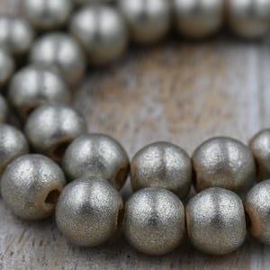 May include: Close-up of a strand of silver-colored beads. The beads are round with a textured surface and a matte finish. The beads are strung together, creating a necklace or bracelet.