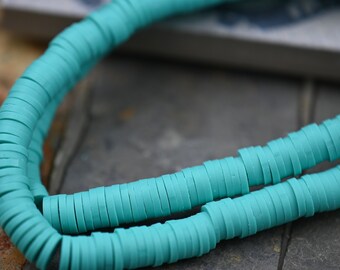 May include: A strand of turquoise blue polymer clay beads. The beads are flat and round, and they are stacked on top of each other.