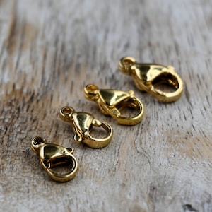 May include: Four gold-toned lobster clasps of different sizes. The clasps are arranged in a row from largest to smallest.