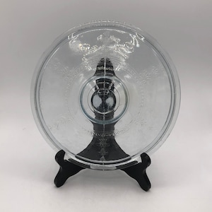 Peut inclure: Une assiette à gâteau en verre transparent avec un motif gravé décoratif. L'assiette est sur un support noir.