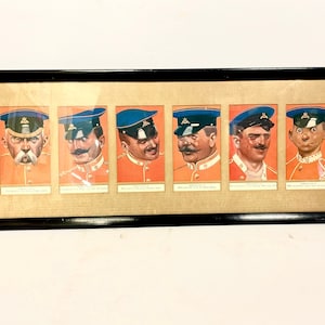 Peut inclure: Une estampe encadrée de six portraits de caricature d'hommes en uniforme militaire. Chaque portrait est dans un cadre séparé et présente un homme différent avec une expression faciale unique et une moustache. Les hommes portent des uniformes rouges et bleus avec des accents dorés.