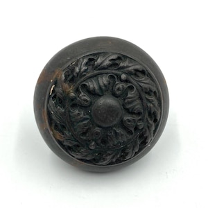 May include: A dark brown, round door knob with a detailed, ornate design of leaves and swirls.