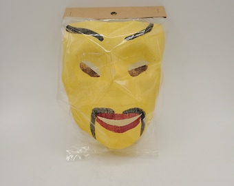 Puede incluir: Una máscara de papel amarilla con cejas, ojos y bigote negros. La máscara tiene una boca roja con un contorno blanco. La máscara está empaquetada en una bolsa de plástico transparente.