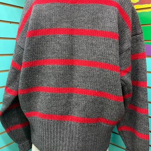 May include: A grey and red striped sweater with long sleeves and a crew neck.