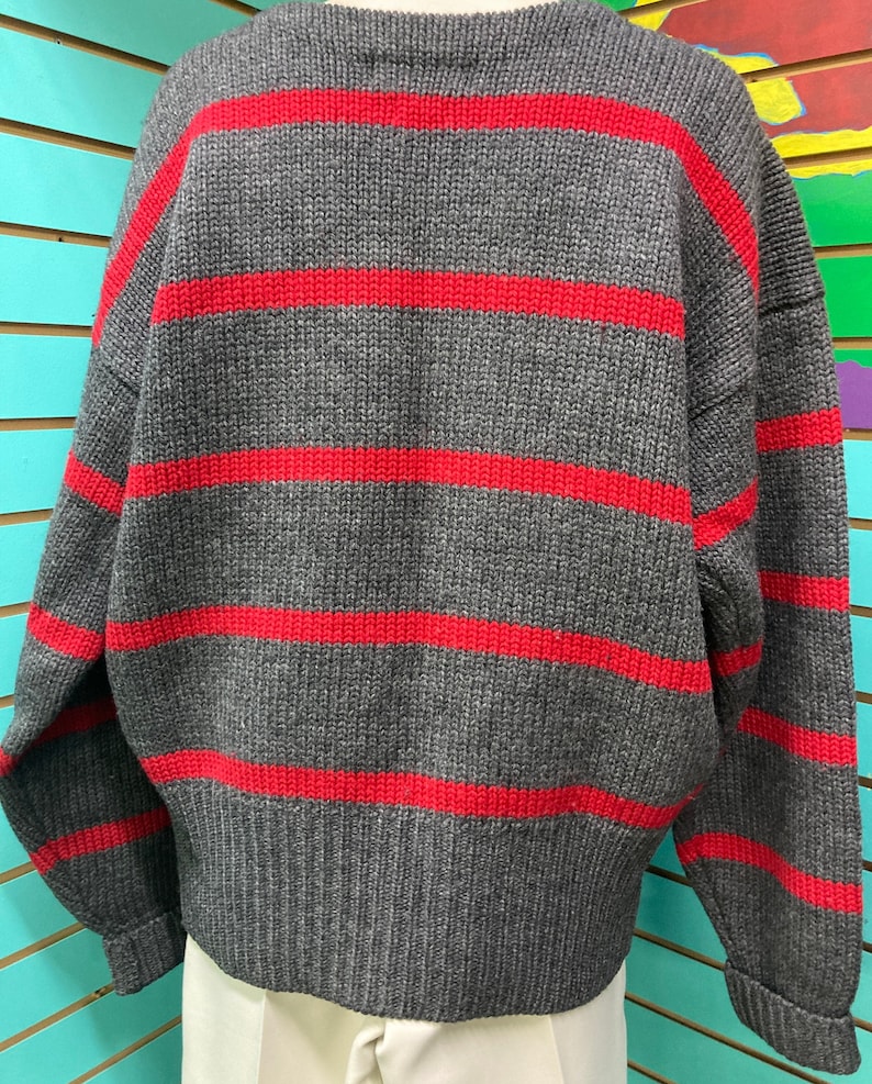 May include: A grey and red striped sweater with long sleeves and a crew neck.