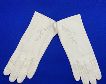 May include: A pair of white leather gloves with delicate floral embroidery. The gloves are long and have a classic style.